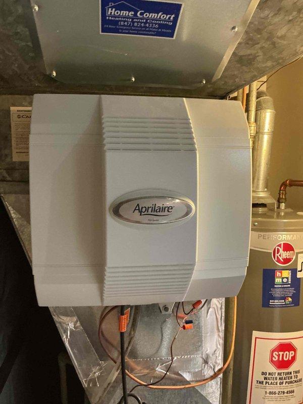 Responded to emergency service call for leaking Aprilaire whole-home humidifier in residential mechanical room. Upon arrival, found humidifier and furnace had been shut off by customer due to active water leak. Performed diagnostic inspection of humidifier unit, including examination of water supply line connections, solenoid valve, drain system, and humidifier pad assembly. Identified source of leak and assessed condition of mounting, ductwork connections, and associated plumbing components. Documented existing equipment configuration with humidifier mounted to HVAC system alongside Rheem water heater in basement utility space. Photographed installation showing flexible ductwork, metallic insulation, and component connections for service records. Evaluated humidifier water panel condition and drainage pathway. Provided customer with repair options and recommendations for resolving leak issue to restore safe humidification operation.