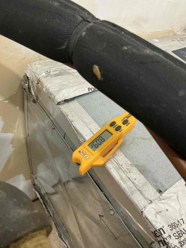 Responded to no cooling complaint on 1-2 year old air conditioning system. Performed diagnostic evaluation of air handler unit and measured operating temperatures using digital thermometer, recording supply air temperature of 93.08°F indicating lack of cooling. Inspected wall-mounted air handling unit with condensate management system and observed evidence of moisture issues with water staining present on surrounding wall surfaces. Evaluated ductwork, condensate piping configuration, and overall system operation to identify cause of cooling failure.