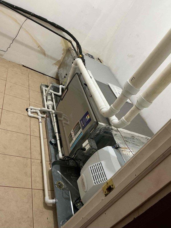 Responded to no cooling complaint on 1-2 year old air conditioning system. Performed diagnostic evaluation of air handler unit and measured operating temperatures using digital thermometer, recording supply air temperature of 93.08°F indicating lack of cooling. Inspected wall-mounted air handling unit with condensate management system and observed evidence of moisture issues with water staining present on surrounding wall surfaces. Evaluated ductwork, condensate piping configuration, and overall system operation to identify cause of cooling failure.