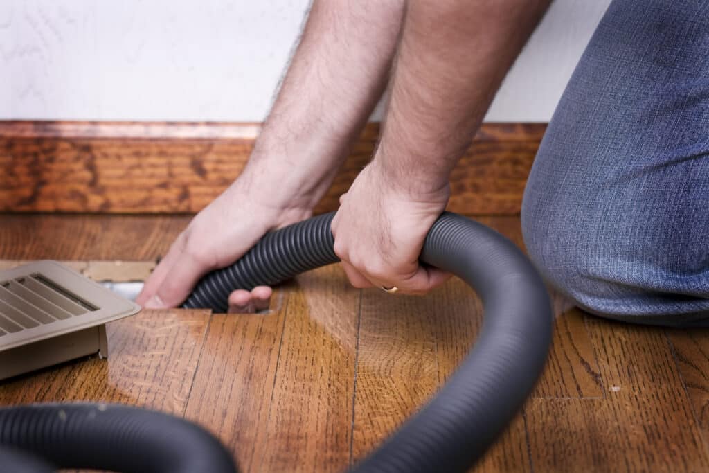 HVAC technician using vacuum to clean residential ducts through air vent