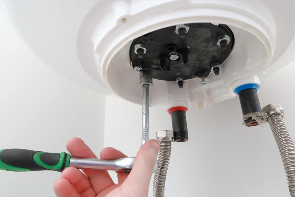 Plumber tightening loose components to fix a boiler leaking water.