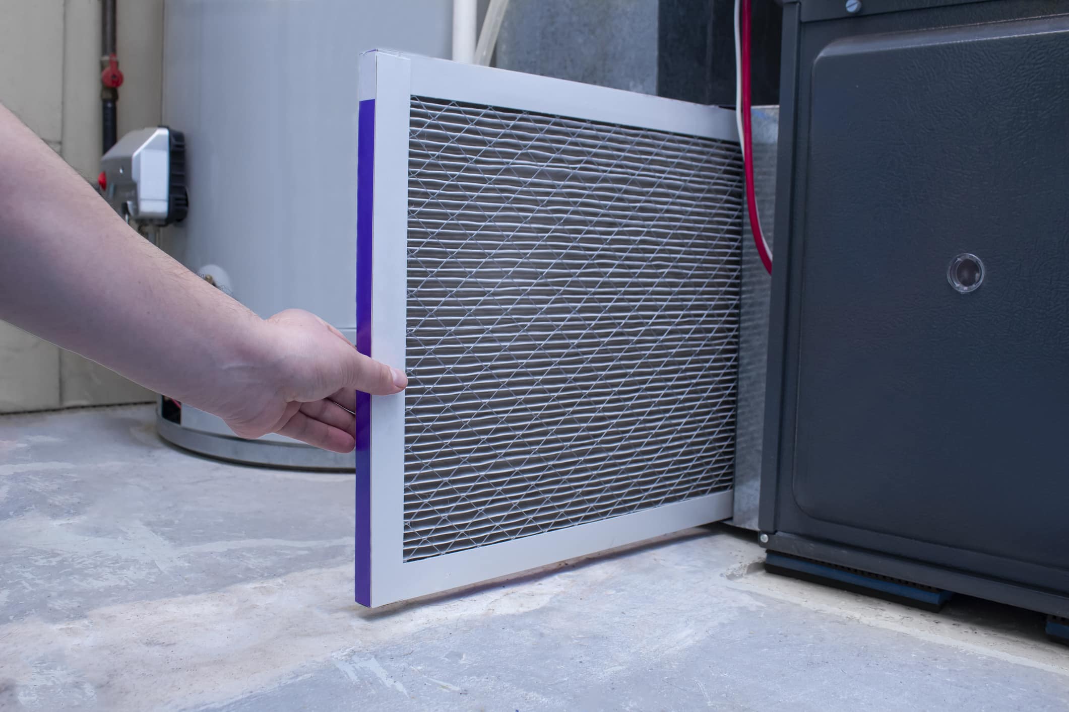 Hand pulling an air filter from a residential furnace